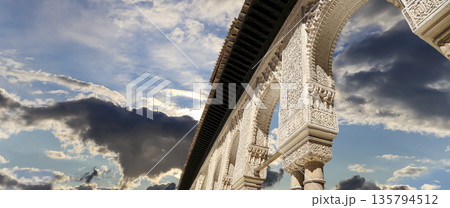 Arches in Islamic (Moorish) style (against the background of a beautiful sky with clouds) in Alhambra, Granada, Spain Arches in Islamic (Moorish) style (against the background of a beautiful sky with clouds) in Alhambra, Granada, Spain 135794512