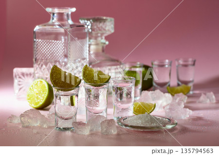 Tequila with lime, sea salt, and crushed ice on a pink background. Tequila with lime, sea salt, and crushed ice on a pink background. 135794563