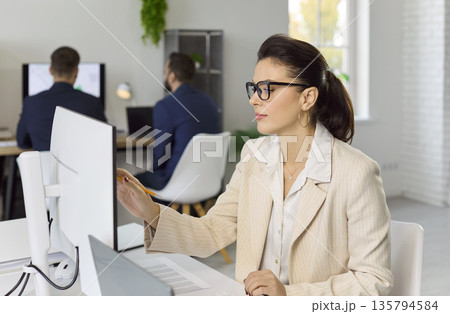 Businesswoman working on accounting software at desktop computer in bright office Businesswoman working on accounting software at desktop computer in bright office 135794584