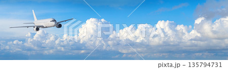 White airplane flying across blue sky with clouds 135794731