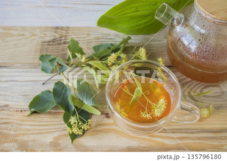 Linden tea in a glass cup with fresh linden flowers, on a wooden background. Medicinal herbal tea. 135796180