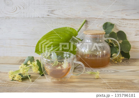 Linden tea in a glass cup with fresh linden flowers, on a wooden background. Medicinal herbal tea. Linden tea in a glass cup with fresh linden flowers, on a wooden background. Medicinal herbal tea. 135796181