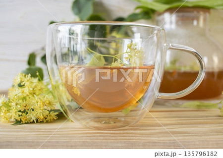 Linden tea in a glass cup with fresh linden flowers, on a wooden background. Medicinal herbal tea. 135796182