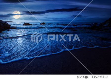 beautiful empty sandy beach at the sea at night. white foam rolling on to the shore near boulder in full moon light. perfect summer vacation concept. awesome weekend mysterious fantasy. low angle beautiful empty sandy beach at the sea at night. white foam rolling on to the shore near boulder in full moon light. perfect summer vacation concept. awesome weekend mysterious fantasy. low angle 135796198