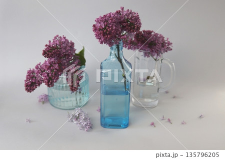 Still life with fresh lilac blossoms in various glass vases. Fresh lilac in a spring composition. 135796205