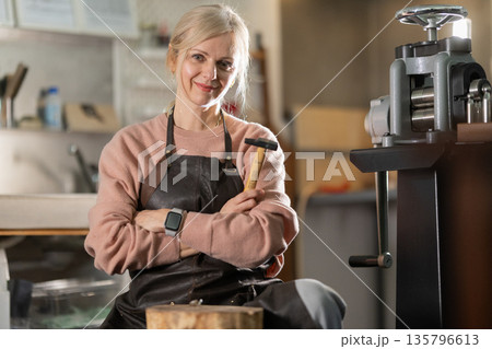 Female artisan confidently holding hammer in jewelry workshop Female artisan confidently holding hammer in jewelry workshop 135796613