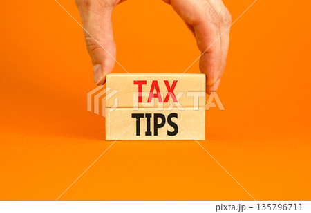 Tax tips symbol. Concept word Tax tips on beautiful wooden blocks. Beautiful orange paper background. Businessman's hand. Business tax tips concept. Copy space. 135796711