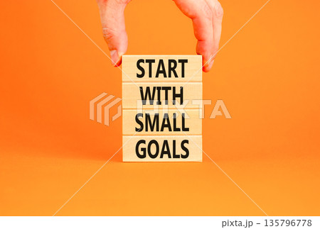 Start with small goals symbol. Concept words phrase Start with small goals on beautiful wooden blocks. Beautiful orange background Businessman's hand Business Start with small goals concept Copy space 135796778