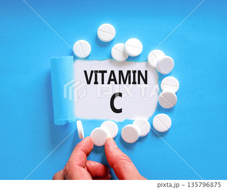 Vitamin C symbol. Concept words Vitamin C on beautiful white paper. White pills tablets. Doctor's hand. Beautiful blue background. Medical healthy lifestyle Vitamin C concept. 135796875