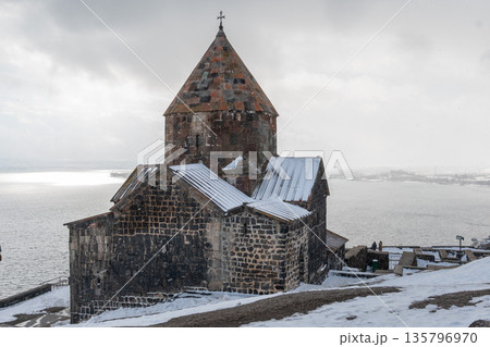 Stone church of Sevanavank Monastery stands above snowy shore of Lake Sevan in Armenia, dark volcanic stone contrasts with icy water Stone church of Sevanavank Monastery stands above snowy shore of Lake Sevan in Armenia, dark volcanic stone contrasts with icy water 135796970