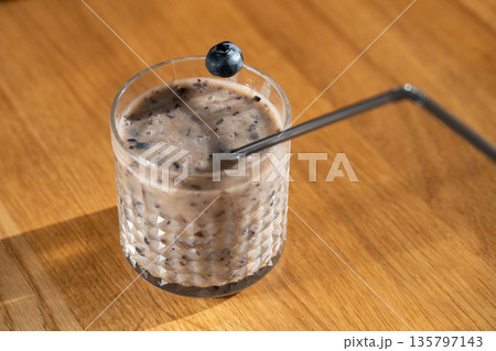 Blueberry falling into glass of smoothie on wooden table Blueberry falling into glass of smoothie on wooden table 135797143