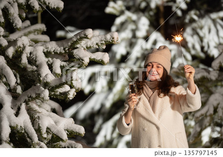 Woman celebrating new year's eve with champagne and sparkler in snowy forest 135797145
