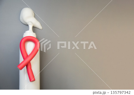 On the side, on a gray background, there is a bottle of foam for long-term hair styling, white foam poured out of it, on it lies a curved pink curler with space for text. The concept of styling 135797342