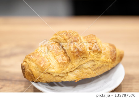 Delicious flaky croissant with crispy outer crust presented on wooden surface under morning sun 135797370