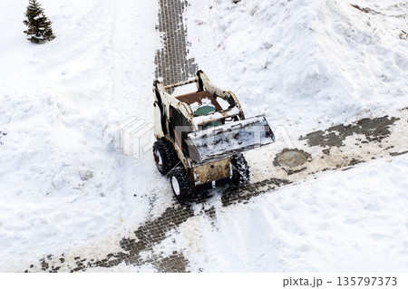Tractor working diligently to clear winter snow and ice from residential streets Tractor working diligently to clear winter snow and ice from residential streets 135797373