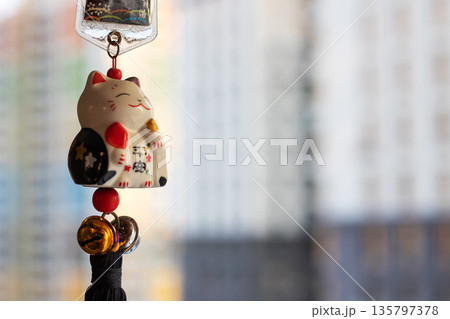 Ceramic lucky cat with charms, Small ceramic charm featuring bells and tassels by window 135797378