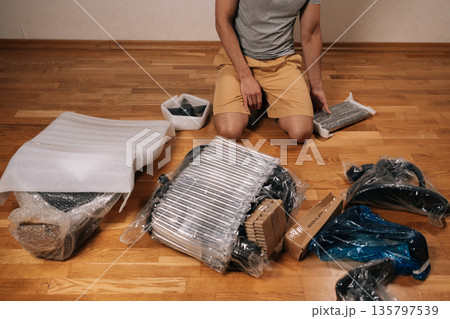 Cropped shot of man kneeling on wooden floor unpacking parts and tools, assembling a new ergonomic office chair at home, following instructions for diy remote-work setup project. Cropped shot of man kneeling on wooden floor unpacking parts and tools, assembling a new ergonomic office chair at home, following instructions for diy remote-work setup project. 135797539