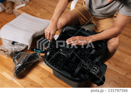 Cropped top view shot of male hands assembling new office chair at home, carefully building furniture parts together for comfort and functionality during work, hobby or gaming sessions. Cropped top view shot of male hands assembling new office chair at home, carefully building furniture parts together for comfort and functionality during work, hobby or gaming sessions. 135797566