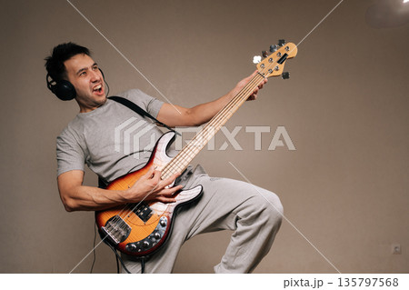 Energetic bassist playing electric guitar with passion and excitement, wearing headphones and enjoying private practice session, showing dedication to music performance. 135797568