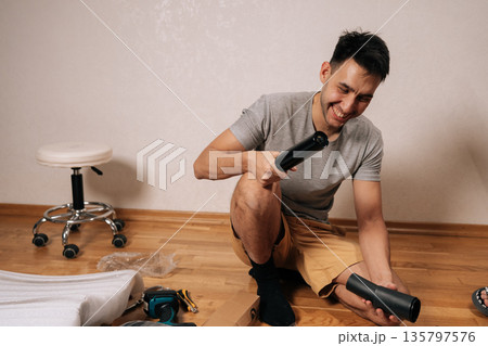Cheerful young man assembling new office chair, sitting on floor, laughing and holding components, engaged in diy furniture construction in home environment. 135797576