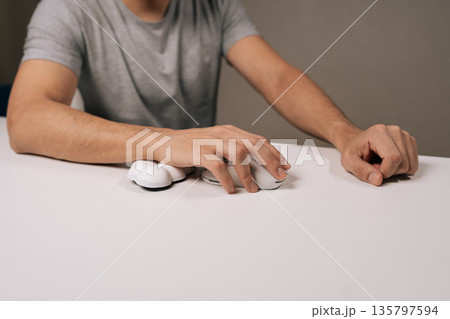 Close-up cropped shot of person using comfortable ergonomic wrist rest and computer mouse on white desk, focusing on wrist support, body posture, and injury prevention in a modern workplace setting. 135797594