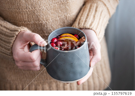A woman holds a mug of non-alcoholic mulled wine or a spicy hot drink with orange 135797619
