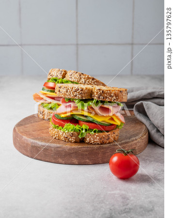 Two sandwiches with ham, cheese, lettuce and vegetable on a wooden board on a concrete background Two sandwiches with ham, cheese, lettuce and vegetable on a wooden board on a concrete background 135797628
