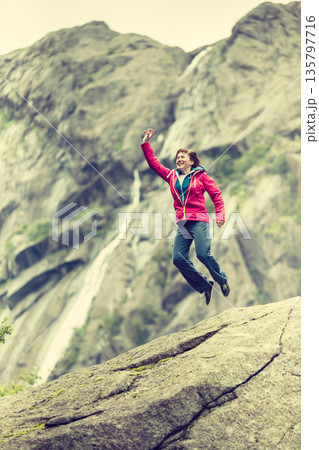 Happy woman jumping on rock in mountains Happy woman jumping on rock in mountains 135797716