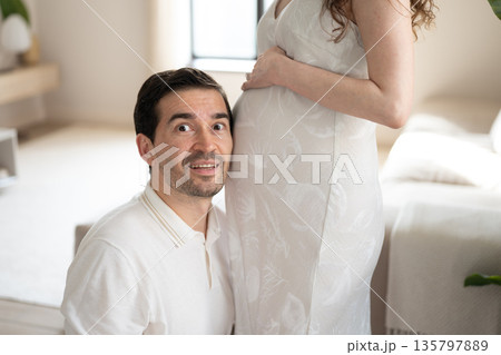 Future father listening to pregnant belly of his wife at home 135797889