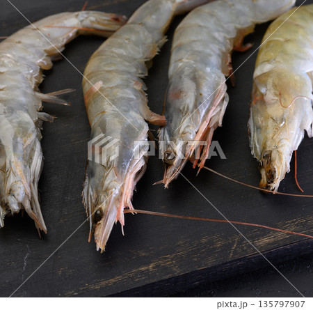Raw shrimps lie in a row on a wooden black board 135797907