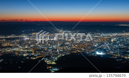 Wide aerial view of a densely built capital illuminated after sunset with streets, neighborhoods and mountain silhouettes in sunset sky, Tirana, Albania 135798670