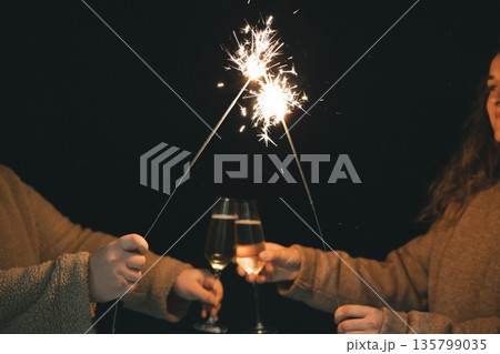 Friends celebrating with sparklers and champagne glasses at night. Festive atmosphere, New Year 2026 and holiday celebration, friendship, joy, party. 135799035