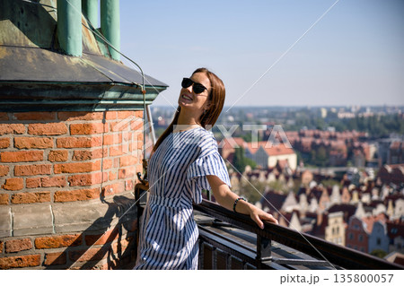 Woman relaxing on rooftop terrace with panoramic view of Gdansk old town 135800057