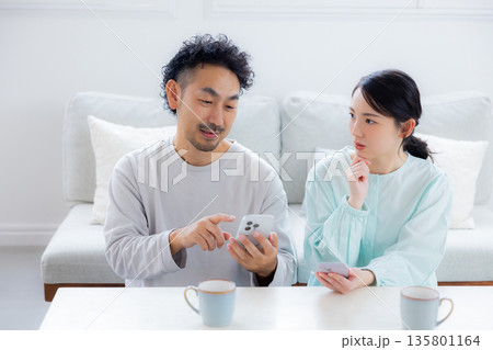 リビングでスマホを見る夫婦 リビングでスマホを見る夫婦 135801164