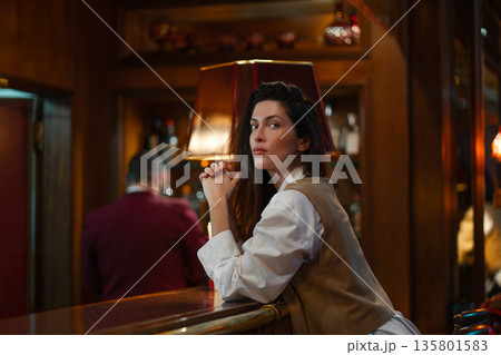 Stylish woman leaning on bar counter in dim lounge Stylish woman leaning on bar counter in dim lounge 135801583