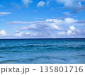 Ocean view under a bright blue sky with scattered white clouds. A rainbow is visible on the horizon, adding a touch of color between the sea and sky 135801716