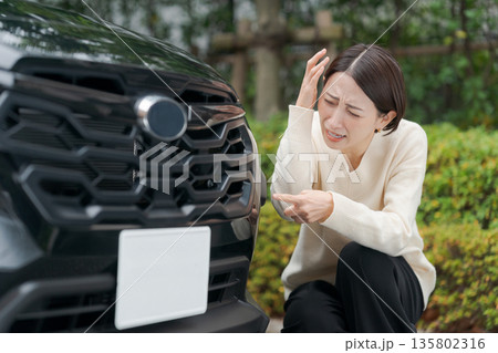 車をぶつけて道にしゃがみ込む女性 135802316