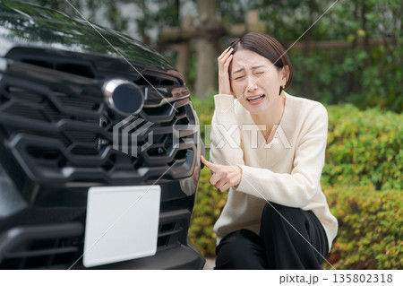 車をぶつけて道にしゃがみ込む女性 135802318