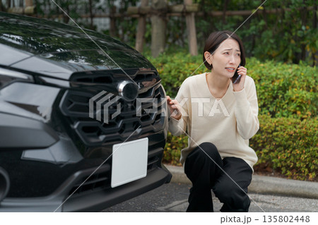 車をぶつけて慌てて電話をする女性 車をぶつけて慌てて電話をする女性 135802448