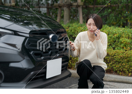 車をぶつけて慌てて電話をする女性 135802449