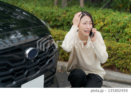 車をぶつけて慌てて電話をする女性 車をぶつけて慌てて電話をする女性 135802450