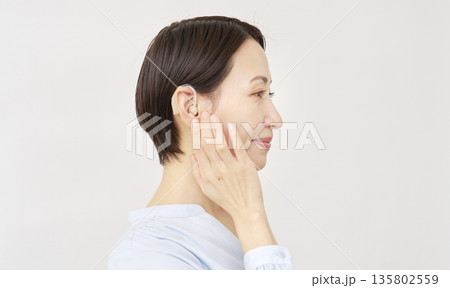 補聴器を使う40代の女性 白背景 補聴器を使う40代の女性 白背景 135802559