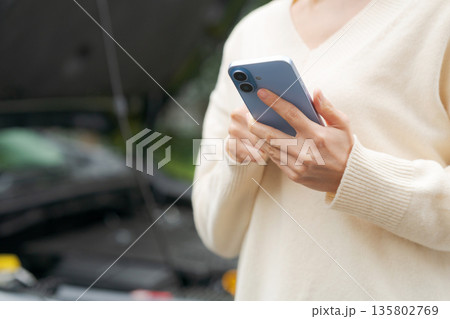 車の前でスマホを操作する女性 135802769