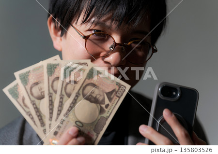 スマホとお金を持つ怪しい男性 スマホとお金を持つ怪しい男性 135803526
