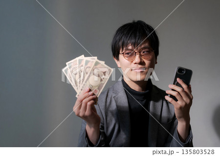 スマホとお金を持つ怪しい男性 135803528