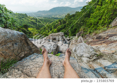 Bare feet at rocky edge of Na Muang Waterfall 2 viewpoint on Koh Samui overlooking tropical jungle valley and distant coastline, travel concept with natural copy space 135803769