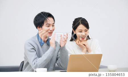 部屋でノートパソコンを見て喜ぶ男女カップル 135804653