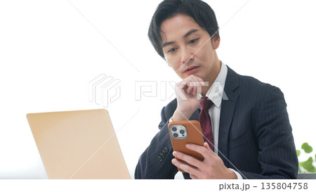 オフィスでノートパソコンとスマホを使う男性ビジネスパーソン オフィスでノートパソコンとスマホを使う男性ビジネスパーソン 135804758