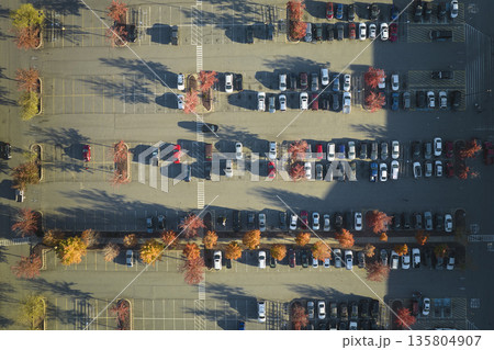 Aerial view of many colorful cars parked on parking lot with lines and markings for parking places and directions. Place for vehicles in front of a strip mall plaza Aerial view of many colorful cars parked on parking lot with lines and markings for parking places and directions. Place for vehicles in front of a strip mall plaza 135804907