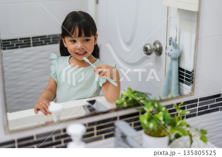 girl child brushing teeth at reflection in mirror in bathroom girl child brushing teeth at reflection in mirror in bathroom 135805525